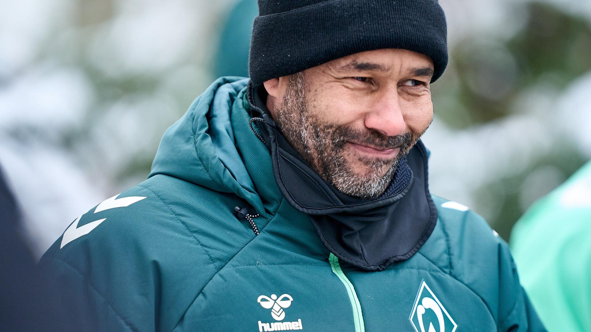 Werders neuer Fußball-Trainer Daniel Thioune geht mit schwarzer Wollmütze lächelnd im verschneiten Bremen zum Trainingsplatz. | Gumzmedia | Andreas Gumz