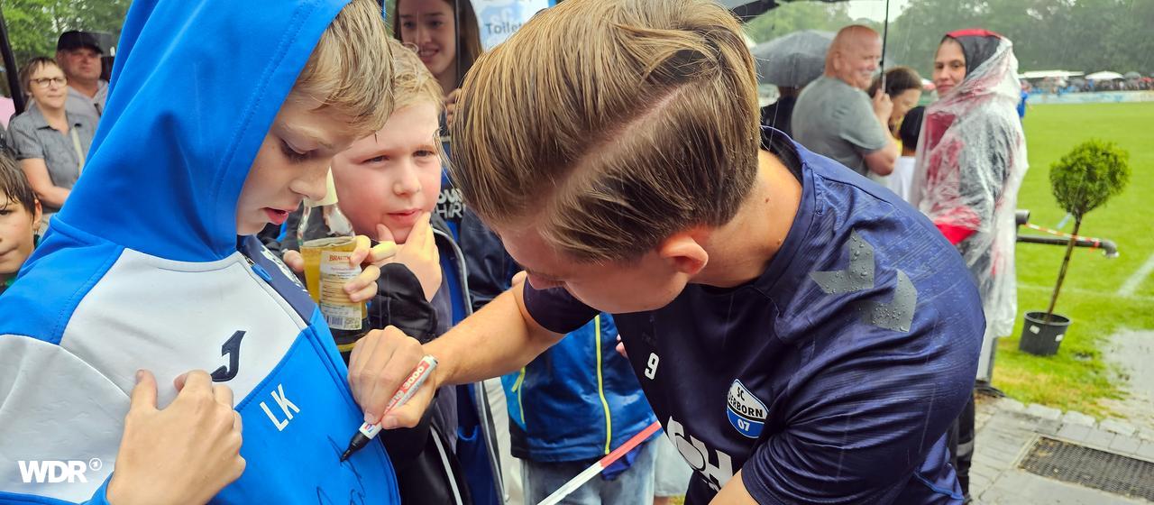 Ein Fußballspieler vom FC Paderborn schreibt sein Autogramm auf den Pulli eines jungen Fans.