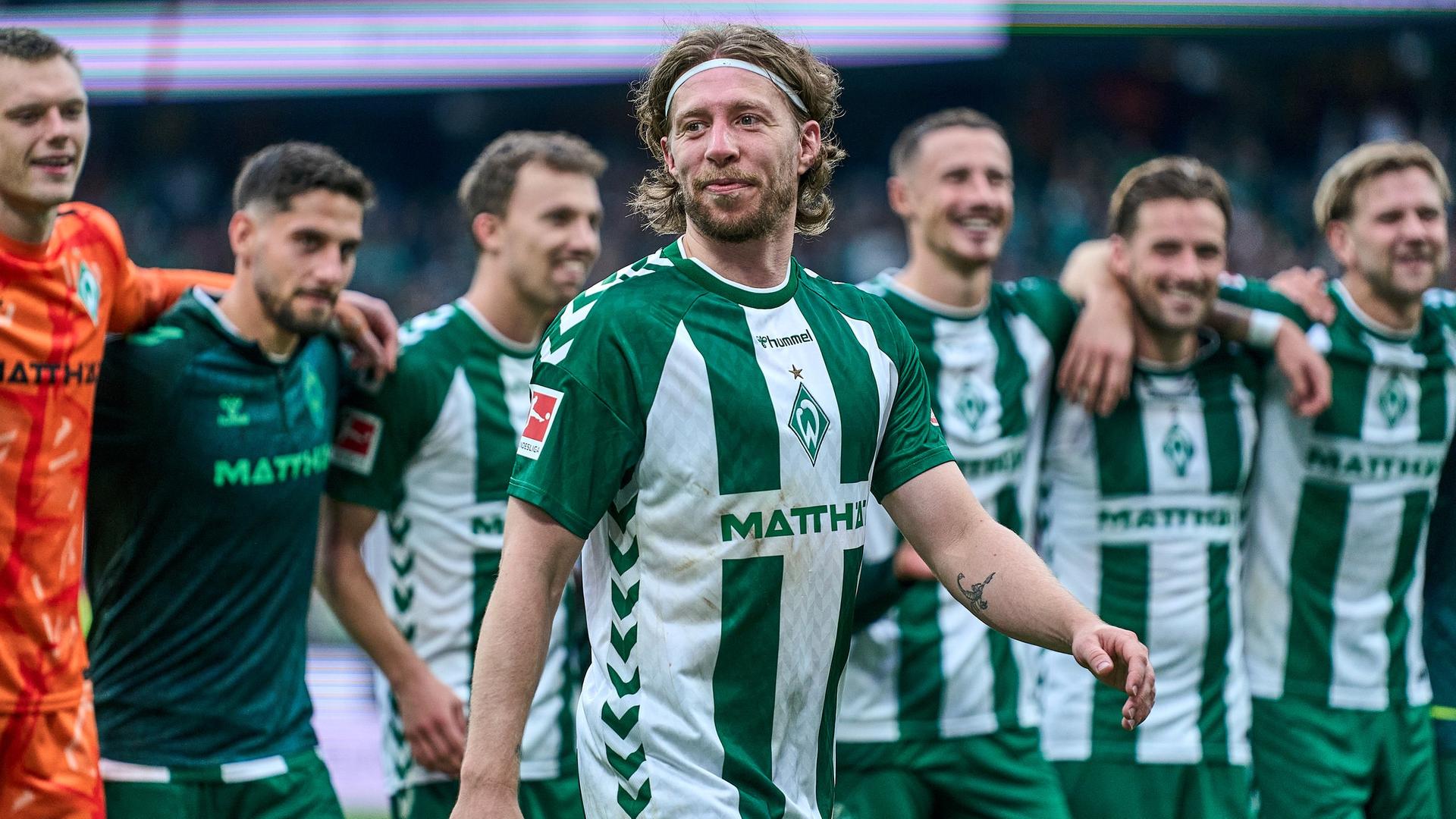 Werders Torschütze Mitchell Weiser steht nach dem Sieg gegen Augsburg strahlend vor der Fankurve, hinter ihm Arm in Arm aufgereiht seine Mitspieler. | Gumzmedia | Andreas Gumz