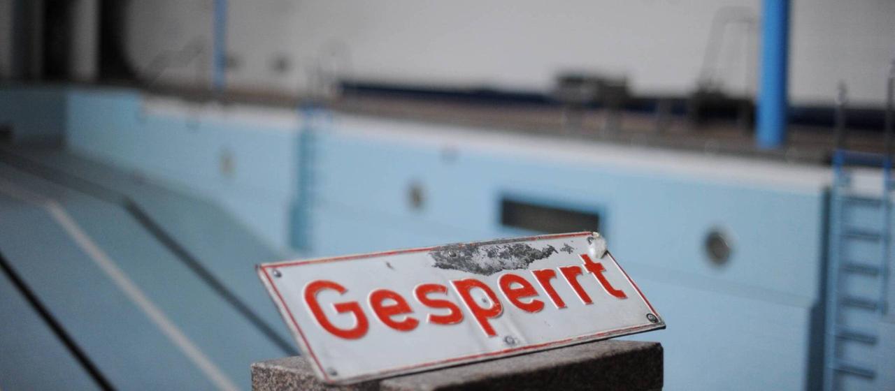 Schild mit der Aufschrift "Gesperrt" vor einem leeren Schwimmbecken