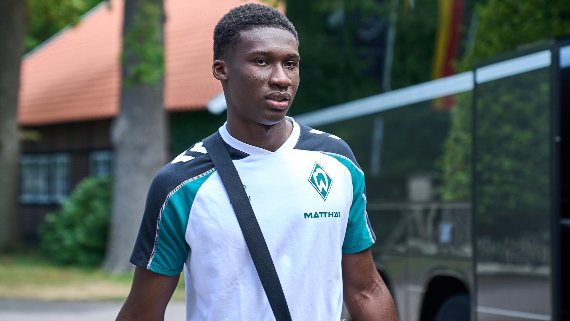 Werder-Profi Karim Coulibaly in Privatkleidung auf dem Weg in den Mannschaftsbus, der vor dem Trainingslager-Hotel in Harsewinkel parkt. | Gumzmedia | Andreas Gumz