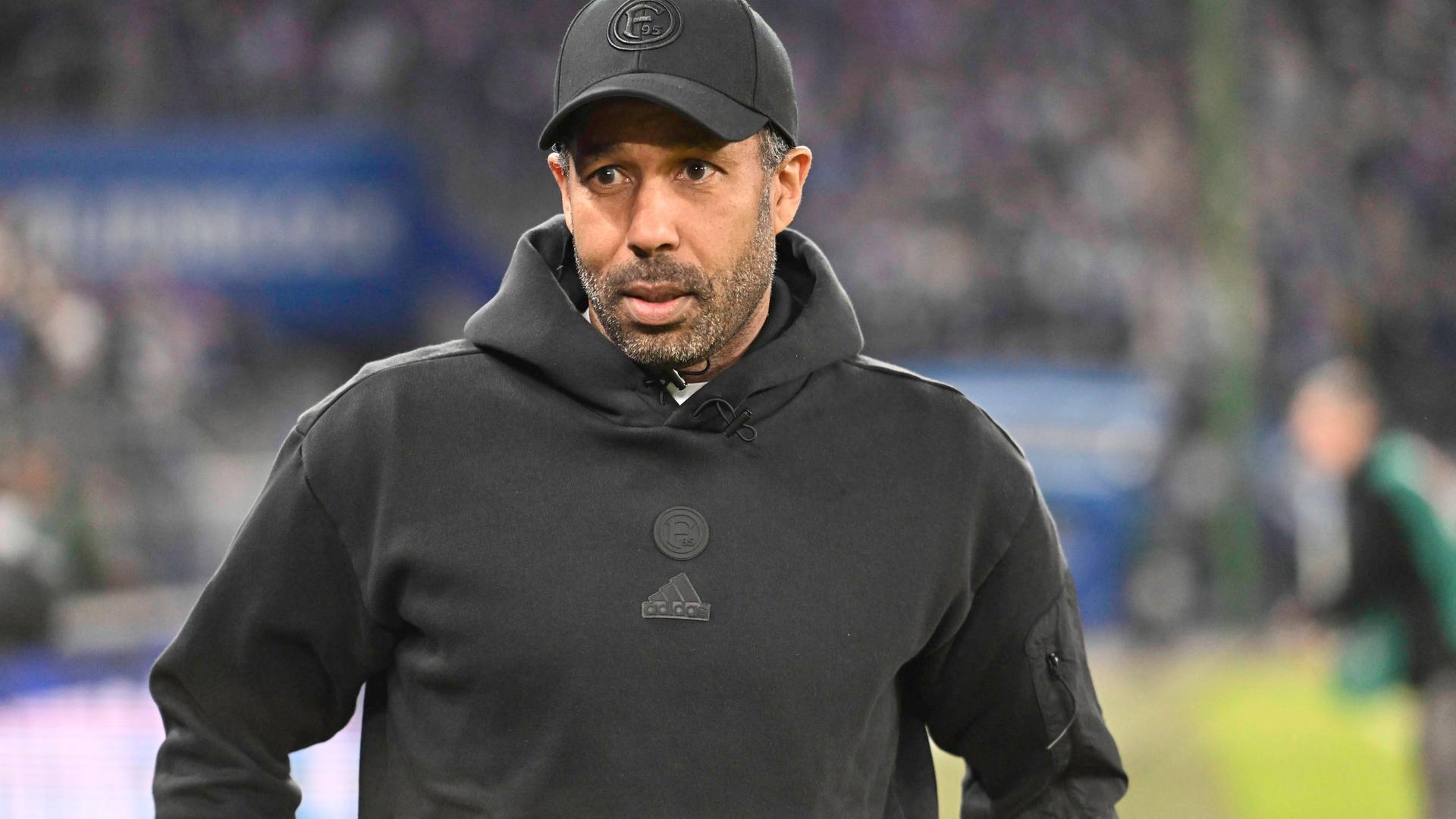 Der Fußball-Trainer von Fortuna Düsseldorf, Daniel Thioune, steht mit schwarzem Kapuzenpullover und schwarzer Kappe am Spielfeldrand im Hamburger Stadion. | Imago | Nordphoto