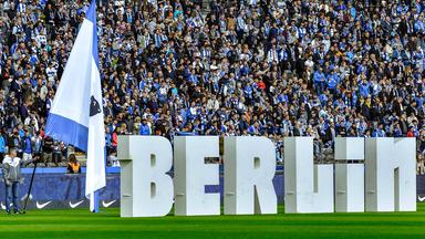 Fans warten vor einem Hertha-Spiel auf den Anpfiff auf dem Rasen steht in großen Buchstaben "Berlin". Quelle: imago images/mix1