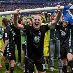 Werders Fußball-Kapitänin Lina Hausicke reckt mit Jubelschrei die Eckfahne mit der HSV-Raute der Fankurve entgegen, hinter ihr alle ihre Mitspielerinnen, die den Einzug ins Pokalfinale feiern.