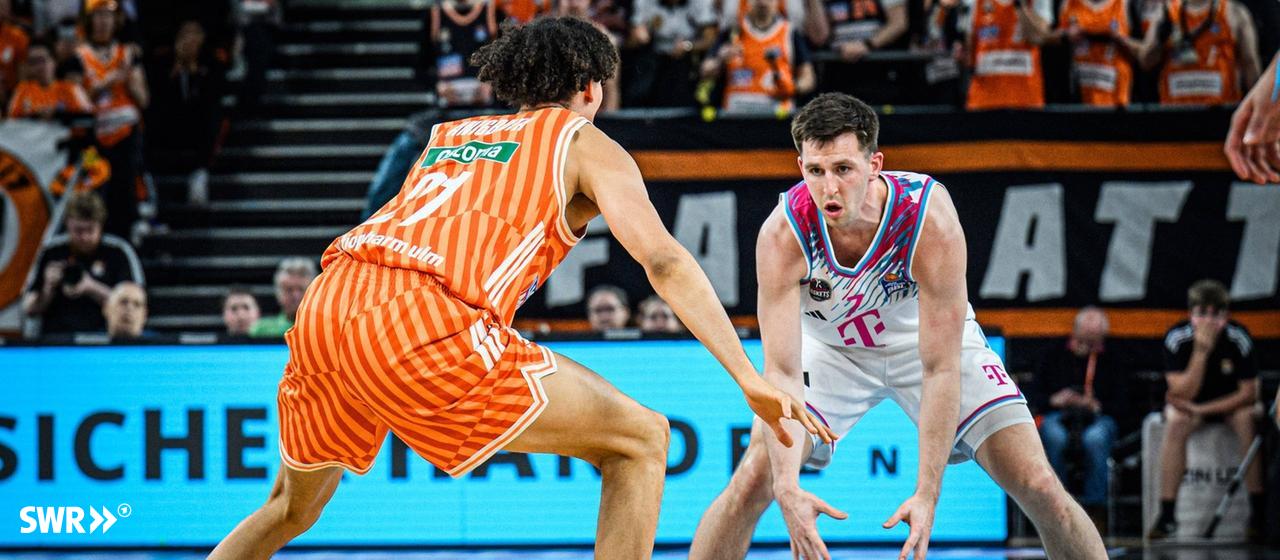 Der Ulmer Spieler Alec Anigbata im orangefarbenen Trikot im Zweikampf mit dem Bonner Grayson Murphy.